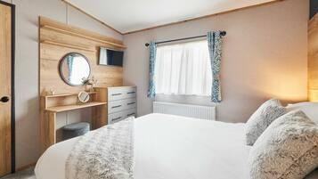 A bedroom with a bed, a dresser, a mirror, a television, and a window with curtains.