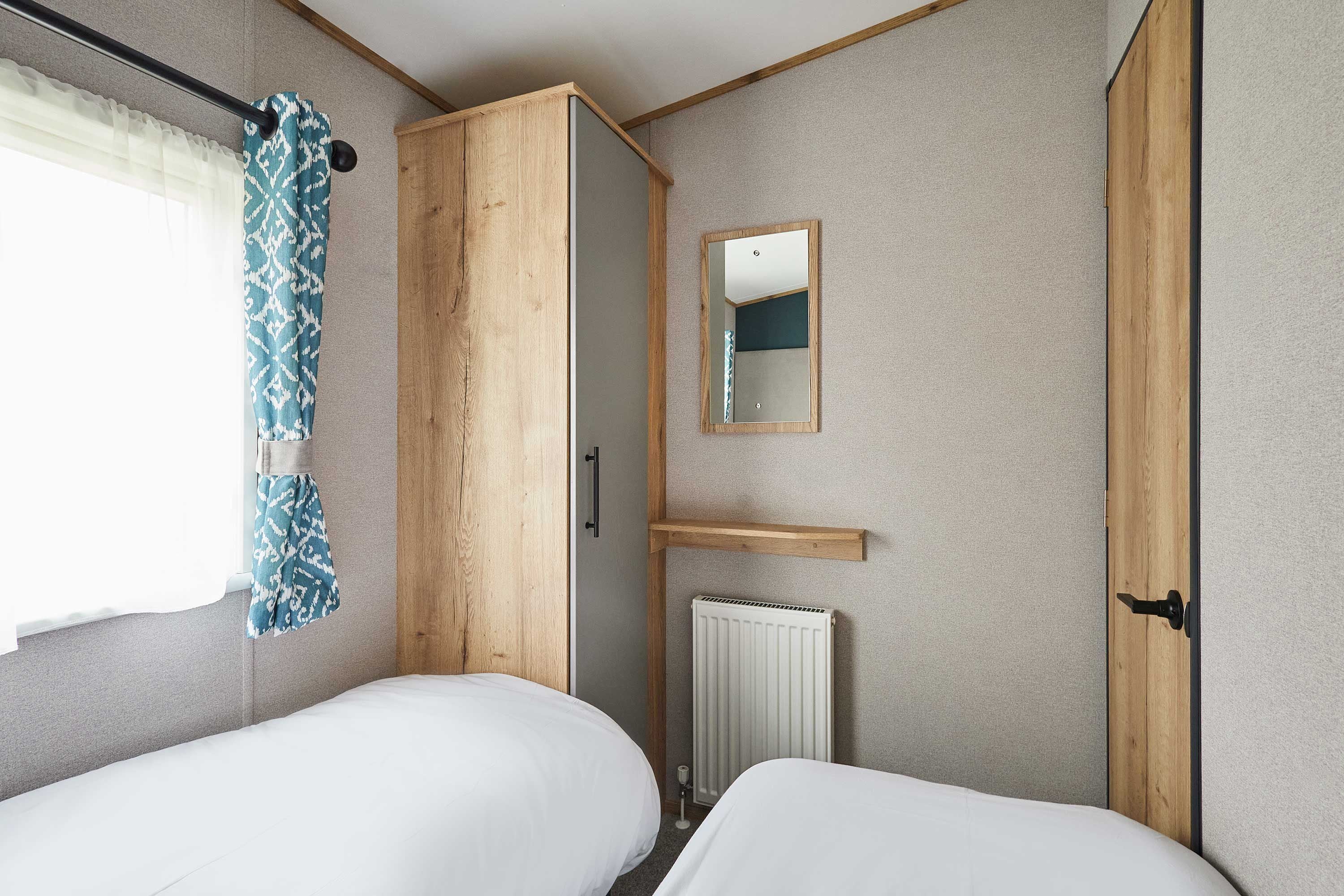 Ein Zimmer mit zwei Betten, einem Kleiderschrank, einem Heizkörper und einem Spiegel an der Wand.