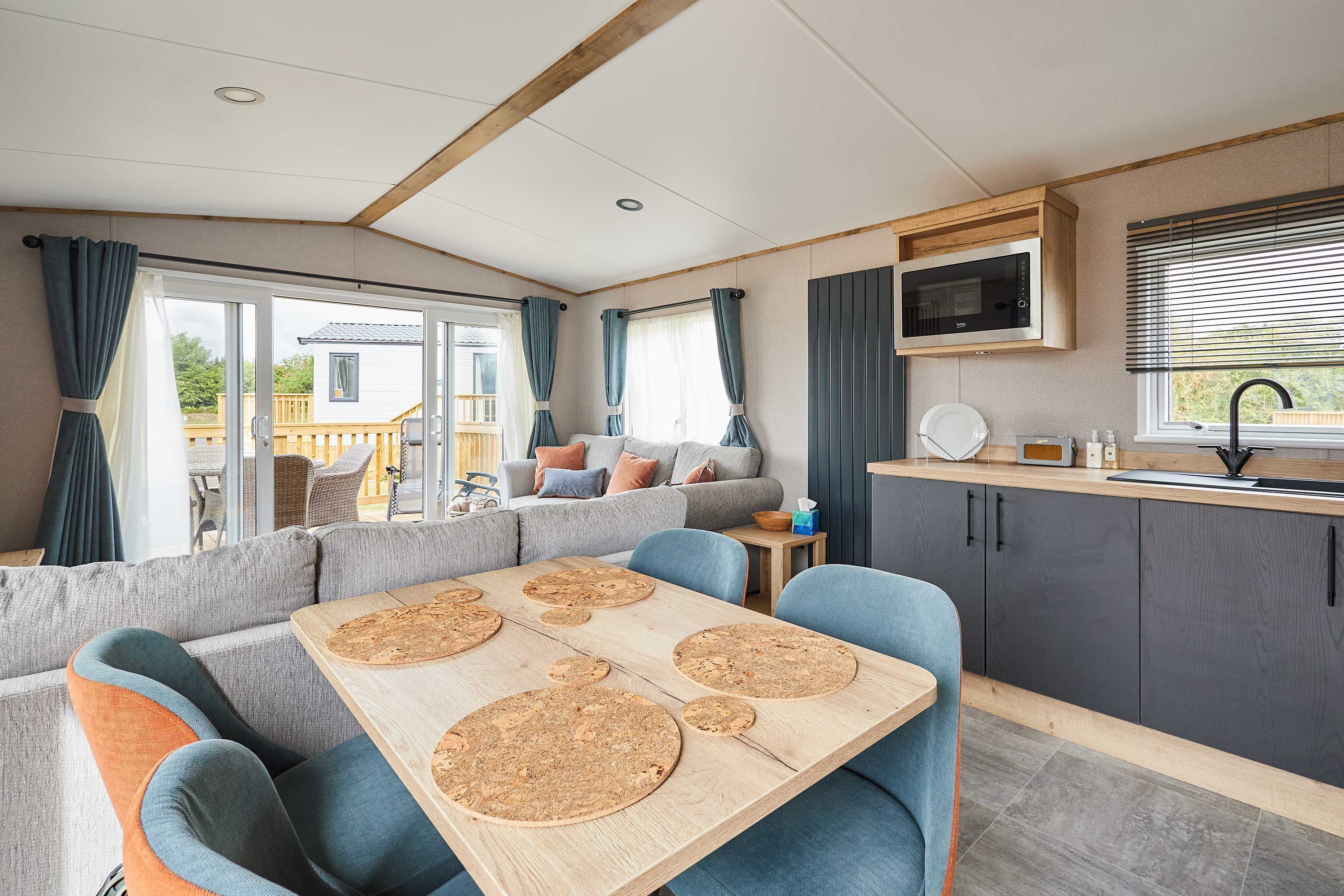 A modern RV interior with a dining area, seating, kitchen, and a view of the outside.