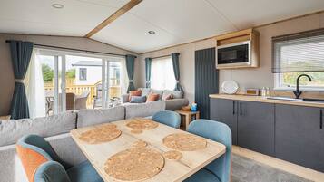A modern RV interior with a dining area, seating, kitchen, and a view of the outside.