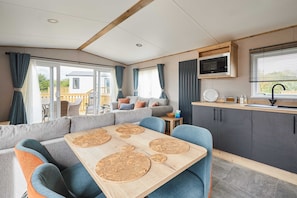 A modern RV interior with a dining area, seating, kitchen, and a view of the outside. - Host Stay Isla II (Pickering)