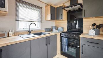 A compact kitchen with a sink, stove, oven, and wooden cabinets.