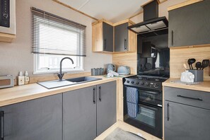 A compact kitchen with a sink, stove, oven, and wooden cabinets. - Host Stay Isla II (Pickering)