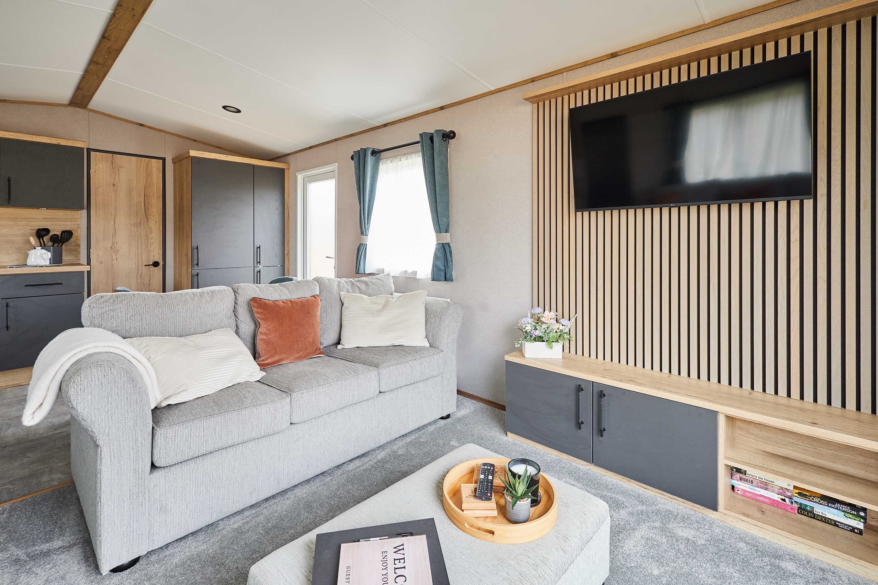 A modern living room with a grey sofa, a wooden cabinet, and a flat-screen TV mounted on a wooden panel wall.