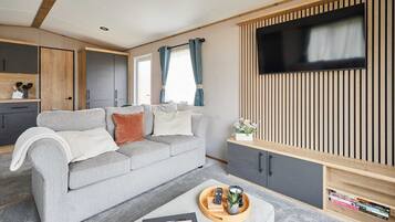 A modern living room with a grey sofa, a wooden cabinet, and a flat-screen TV mounted on a wooden panel wall.