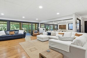 A modern living room with a large sofa set, a coffee table, and a dining area visible through glass doors. - Mountain Song-Hot Tub+Sauna+Arcade Gms+Fenced Yard (Maggie Valley)
