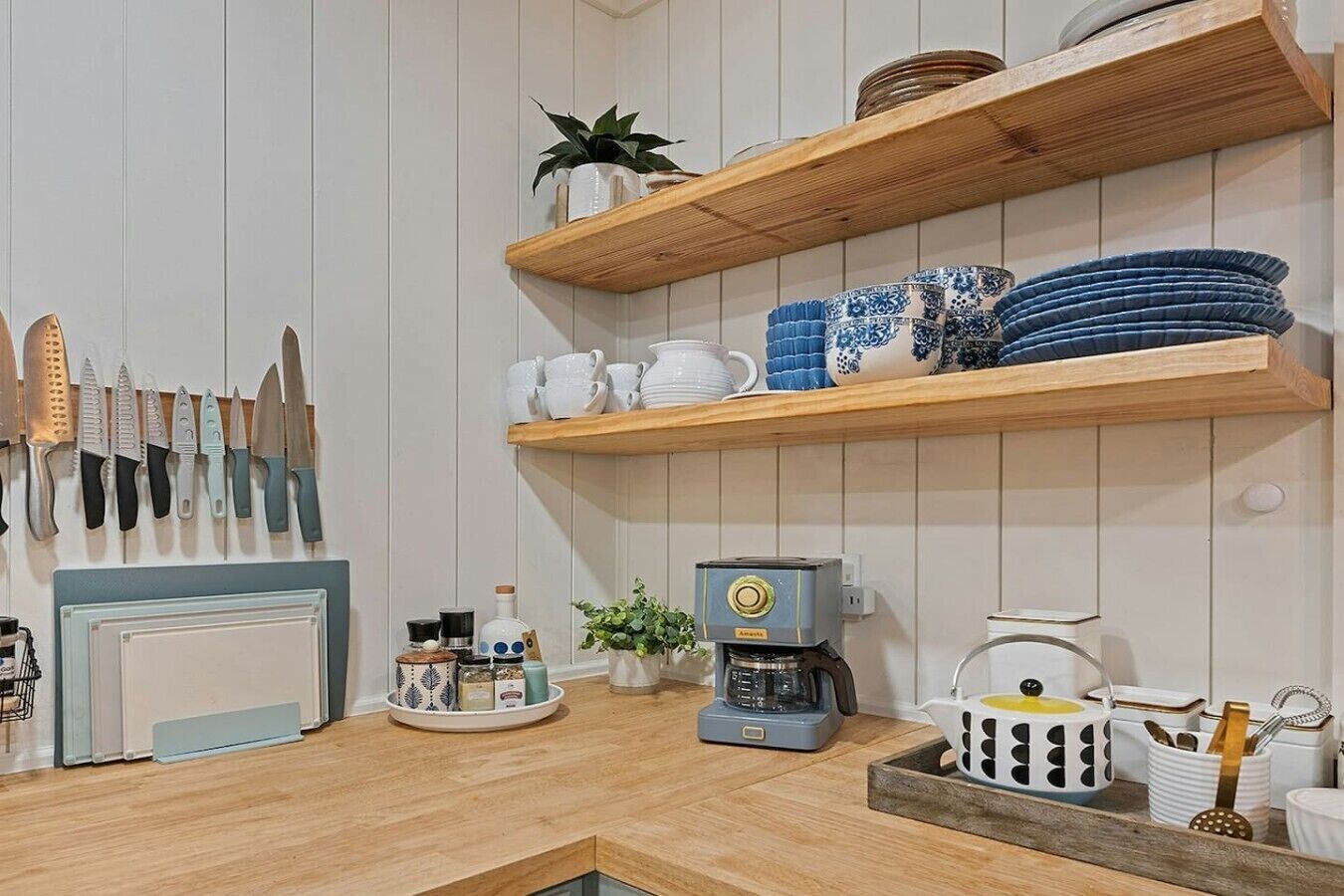 A kitchen with wooden shelves holding dishes and utensils, a coffee machine, and a variety of kitchen tools.
