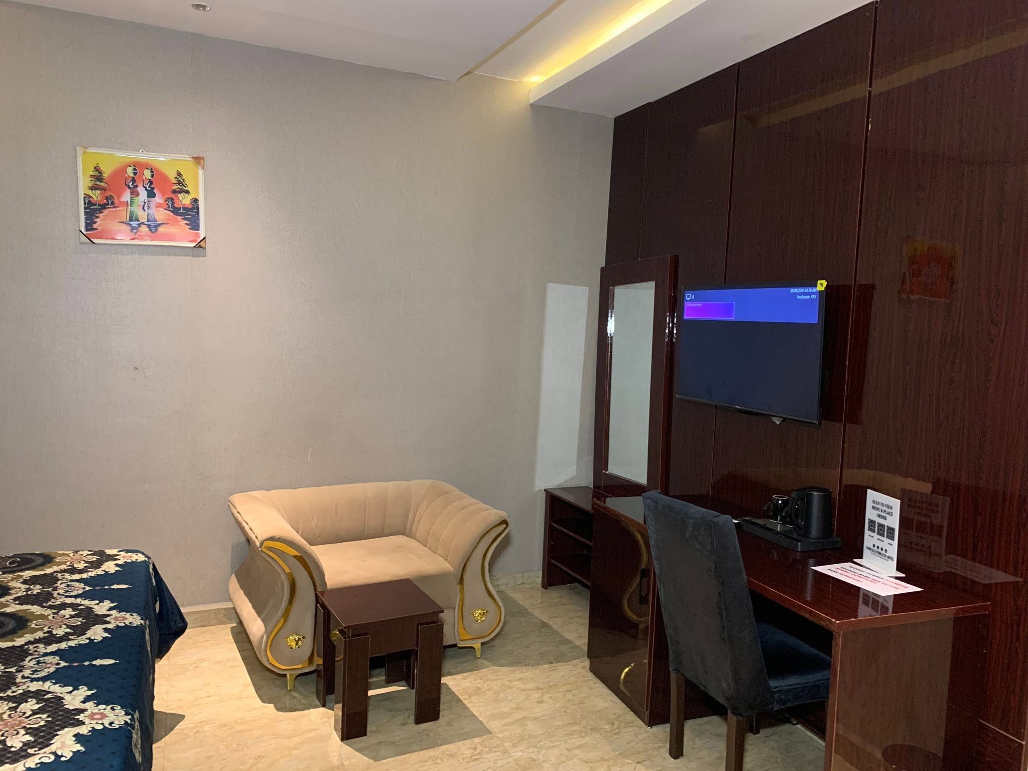 A hotel room with a sofa, a small table, a desk with a chair, a television, and a wall-mounted mirror.