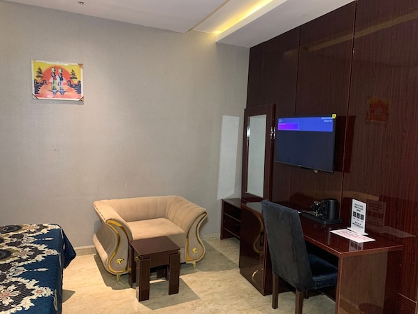 Habitación de hotel con sofá, una pequeña mesa, escritorio con silla, televisor y espejo montado en la pared.