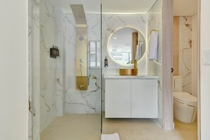 Ein modernes Badezimmer mit einer gläsernen Dusche, einer Marmorwand und einem runden Spiegel.