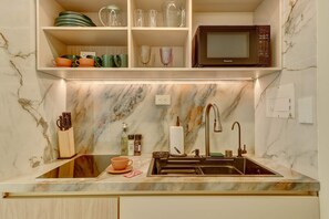 Cozinha com painel de parede de mármore, pia com torneira moderna e micro-ondas sobre a bancada.