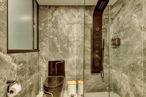 Ein Badezimmer mit Marmorwand, Toilette, Bidet, Dusche und Spiegel.