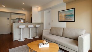 A modern living room with a sofa, a coffee table with a book, and a kitchen area with bar stools. - w Enchanting 1BR w Balcony in Prime Miraflores (Lima)