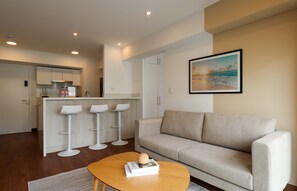 Una sala de estar moderna con un sofá, una mesita de centro con un libro y una zona de cocina con taburetes de bar.