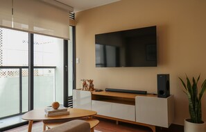 Una sala de estar moderna con una televisión de pantalla plana montada en la pared, una mesa de centro de madera, un sofá y una planta en maceta.