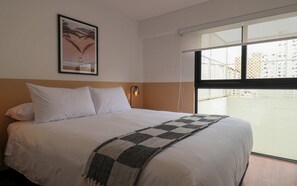 Habitación de hotel con cama, un cuadro en la pared, una ventana con vistas y una luz nocturna.
