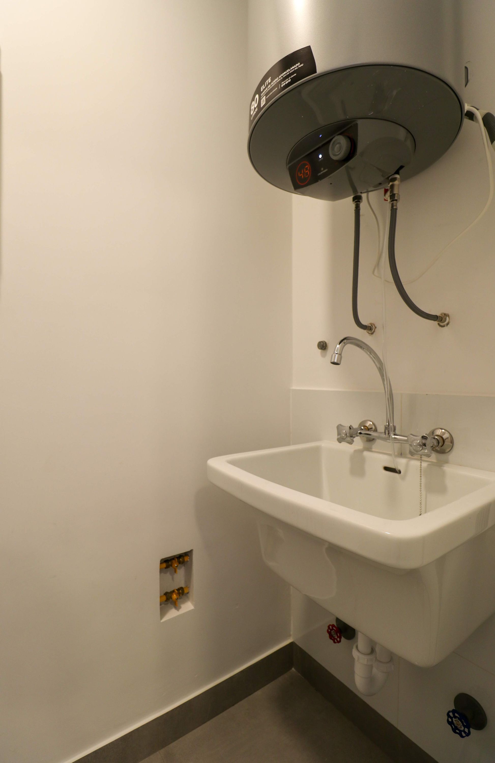 A bathroom with a white sink, a handheld showerhead, and a wall-mounted heater.