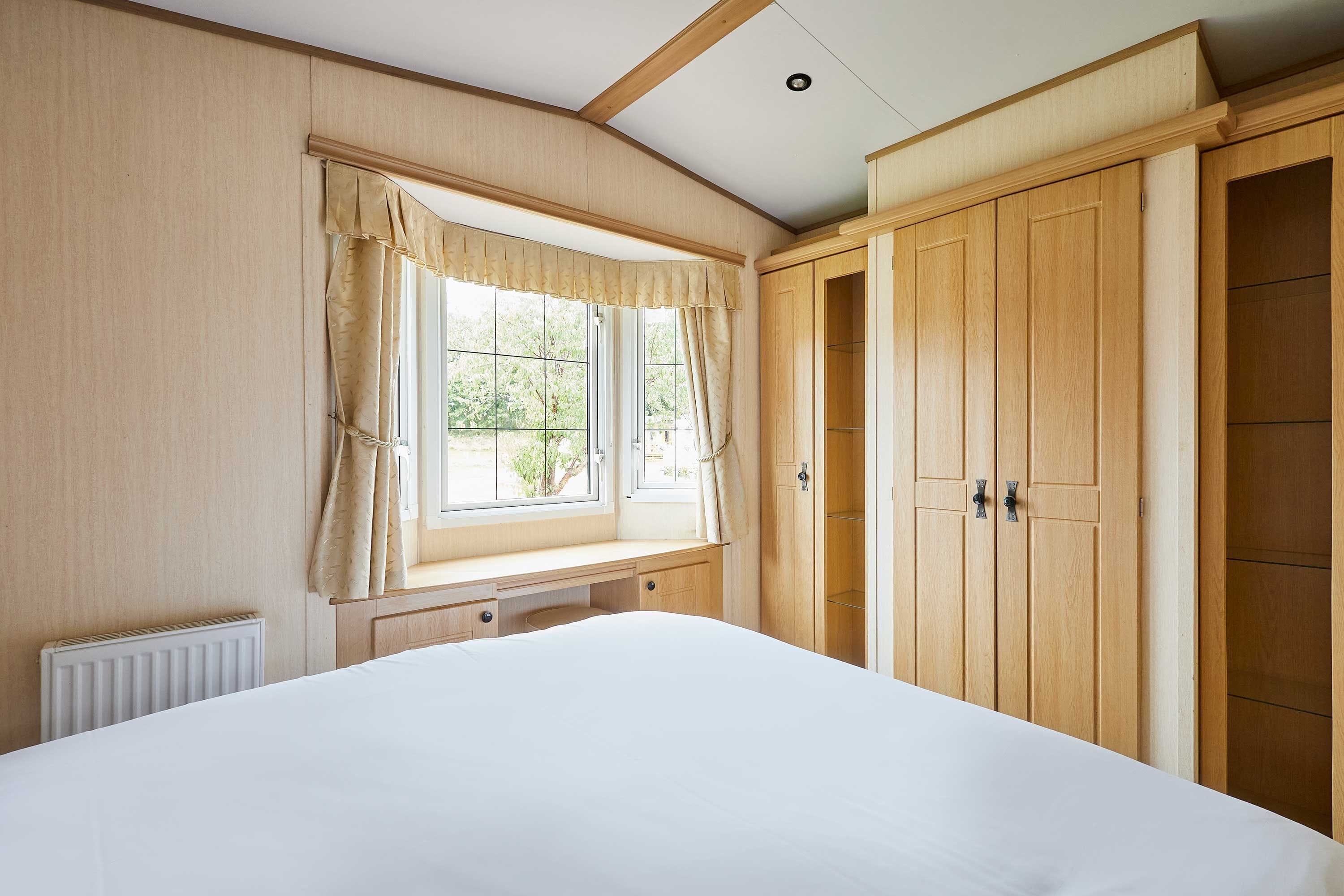 Une chambre à coucher avec un lit, une fenêtre avec des rideaux, un radiateur et des portes de placard en bois.
