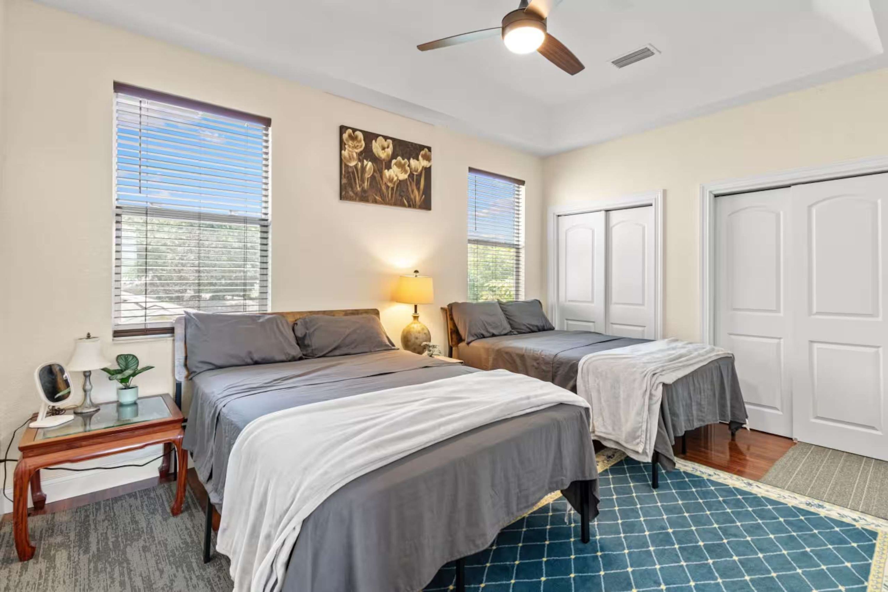 A bedroom with two beds, a ceiling fan, and a window with blinds.