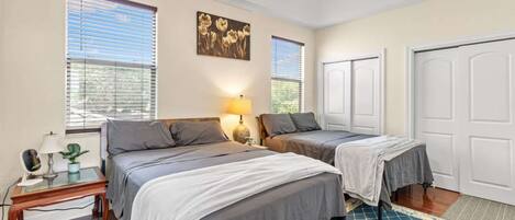 A bedroom with two beds, a ceiling fan, and a window with blinds.
