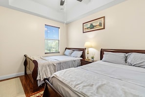 A hotel room with two single beds, a window with blinds, a bedside table with a lamp, and a painting on the wall. - 4BR Escape 10 Mins to Madeira Clearwater Beach (Pinellas Park)