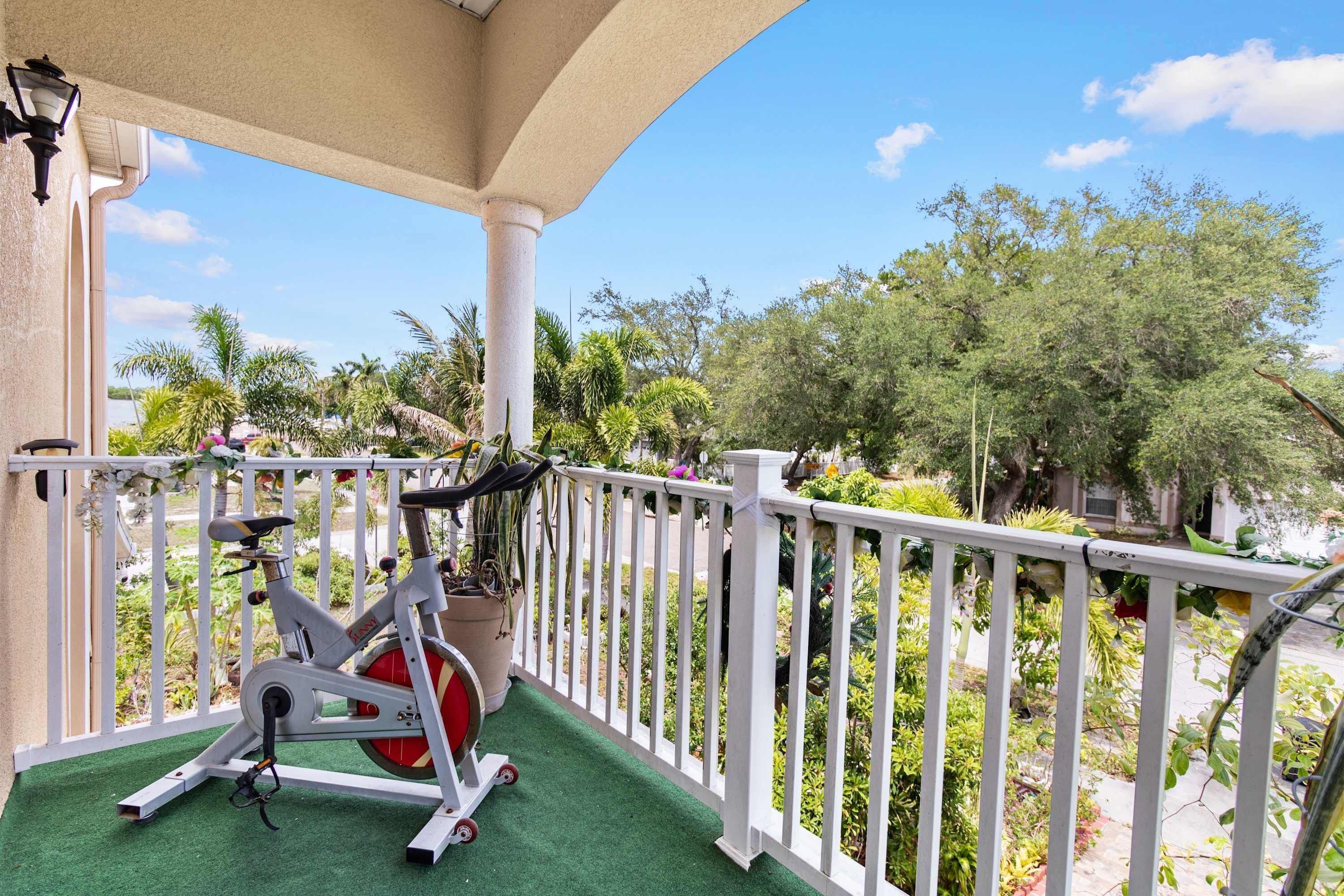 Un balcon équipé d’un vélo d’appartement, doté d’une balustrade blanche et offrant une vue sur les arbres et un ciel dégagé.