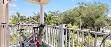 Un balcon équipé d’un vélo d’appartement, doté d’une balustrade blanche et offrant une vue sur les arbres et un ciel dégagé.