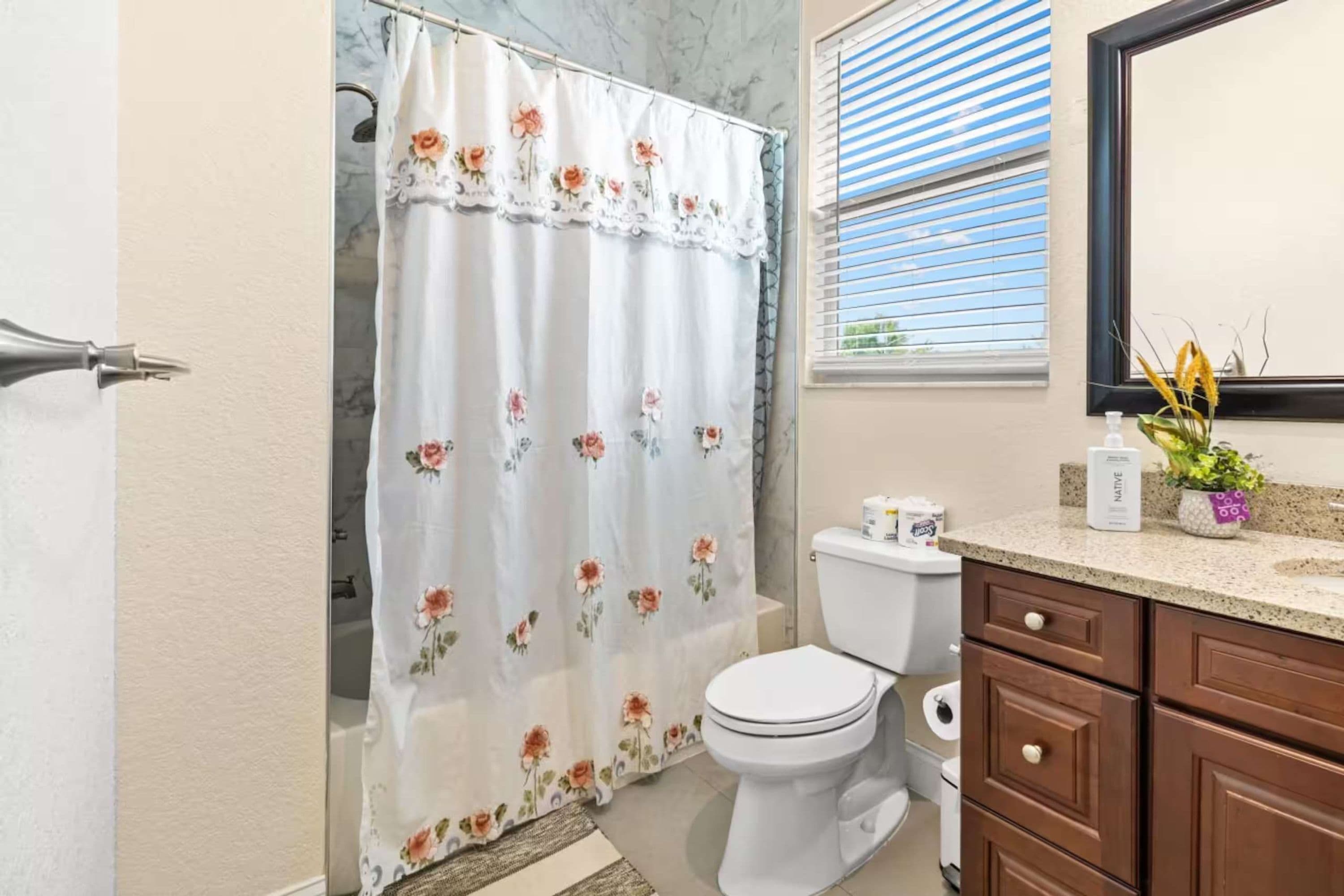A bathroom with a shower curtain, toilet, sink, and mirror.