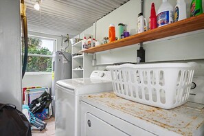 Uma lavanderia com máquina de lavar, secadora e prateleira com produtos de limpeza.