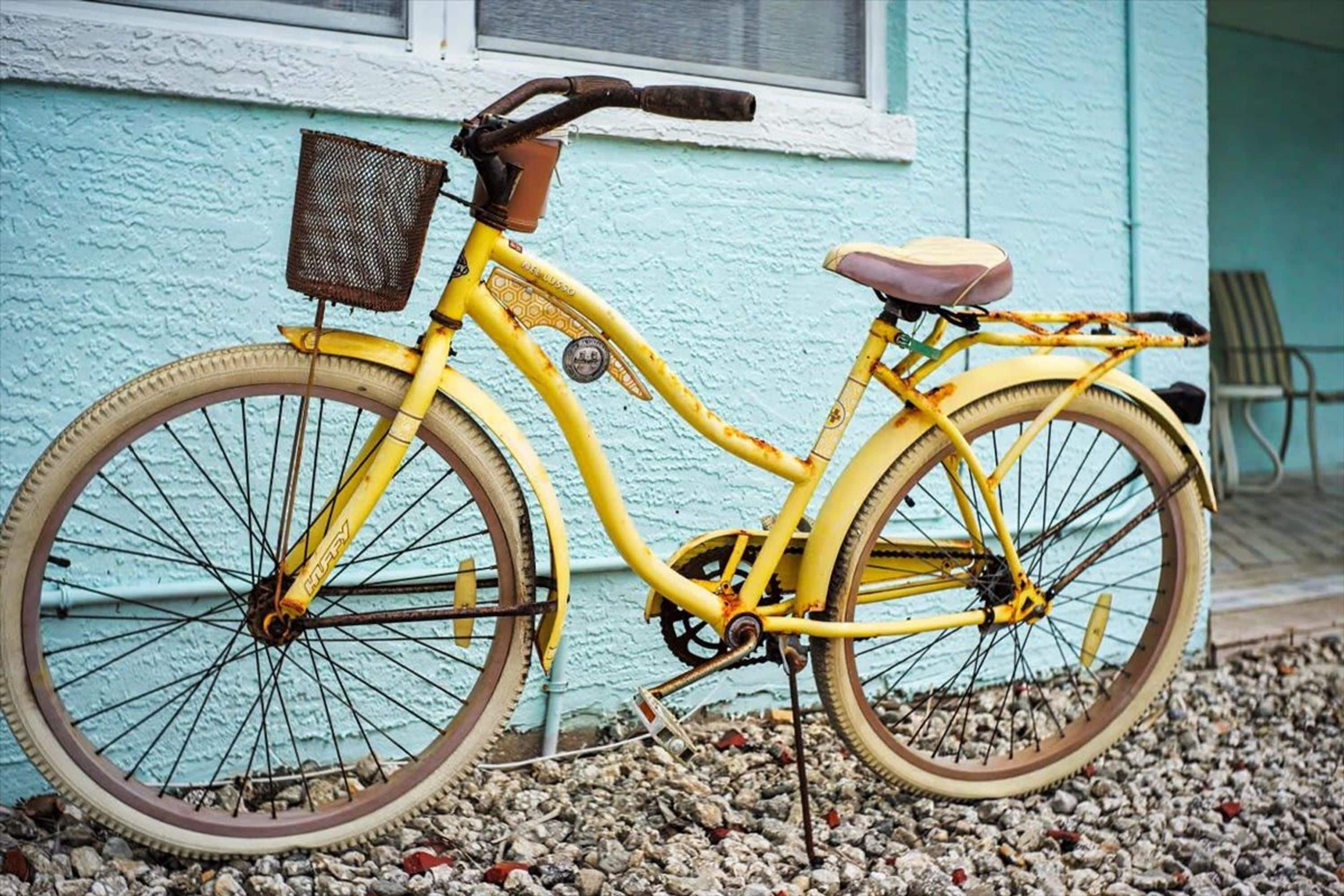 A yellow bicycle parked on gravel in front of a building with a blue exterior.