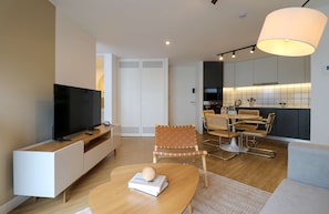 Uma sala de estar moderna com uma televisão de tela plana, uma mesa de centro de madeira e uma área de jantar com mesa e cadeiras.