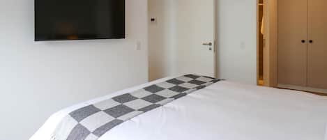 A bedroom with a bed, a television mounted on the wall, and a wardrobe.