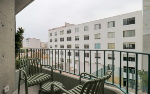 Ein Balkon mit zwei grünen Stühlen, einem Metallgeländer und Blick auf ein weißes Gebäude mit zahlreichen Fenstern.