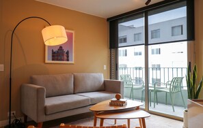 Uma sala de estar moderna com sofá, mesa de centro, abajur e uma janela grande com vista para a cidade.