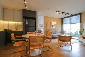 Uma sala de estar moderna com uma mesa de jantar redonda, cadeiras de vime, um sofá e uma grande janela com vista.