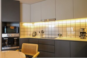 Eine moderne Küche mit grauen Schränken, einer Edelstahl-Dunstabzugshaube, einer Mikrowelle, einer Kaffeemaschine und einem Korbstuhl.