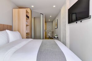 A modern hotel room with a large bed, a wooden wardrobe, a television mounted on the wall, and a small desk with a chair. - w Refined Loft w Balcony in Usaquen (Bogotá)