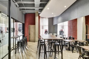 A modern dining area with long tables and chairs, a wooden floor, and a red accent wall. - w Refined Loft w Balcony in Usaquen (Bogotá)