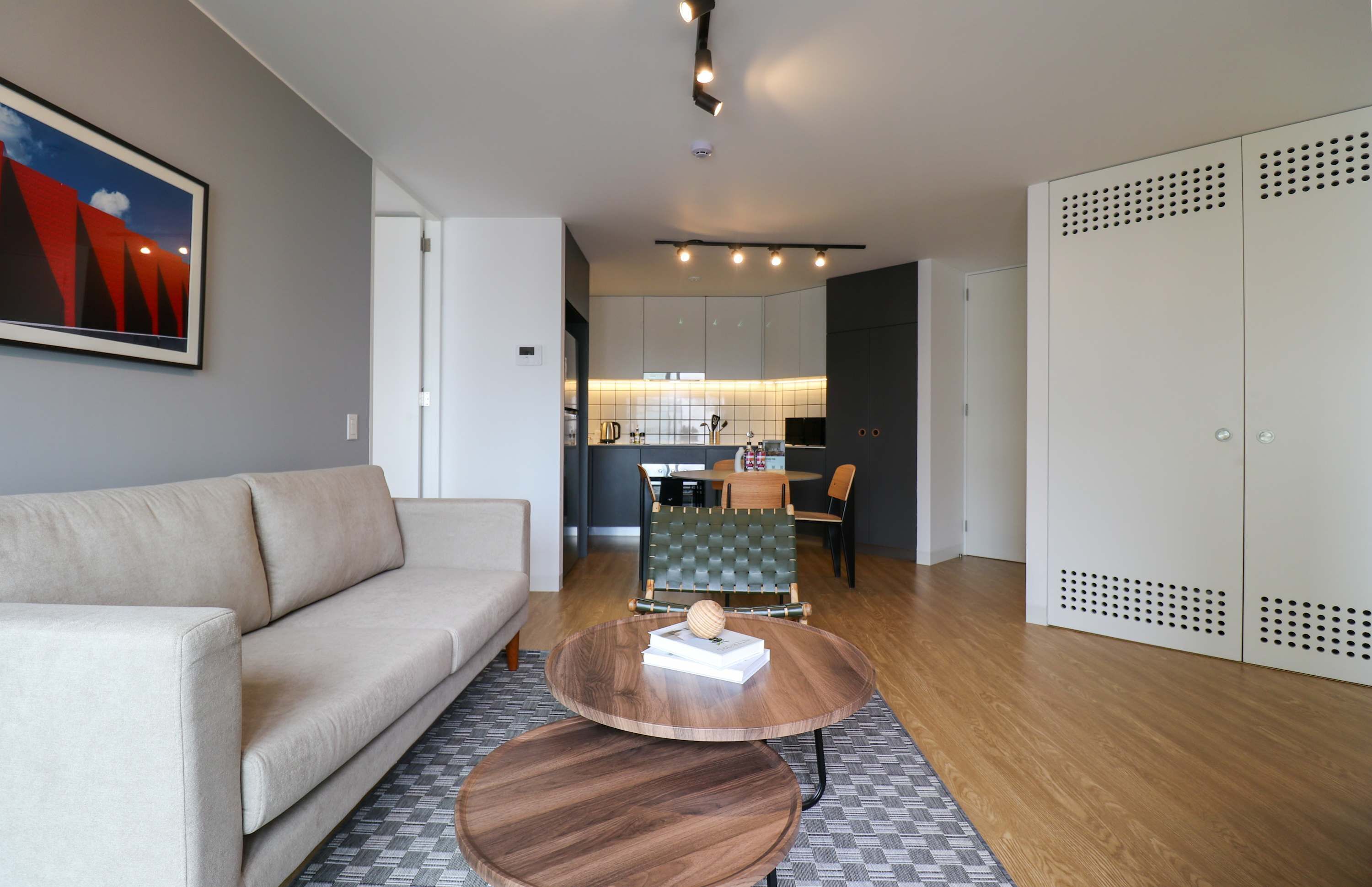 A modern living room with a sofa, two round wooden tables, and a kitchen in the background.