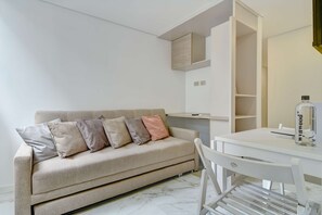 Quarto minimalista com sofá, escrivaninha e uma garrafa de água.