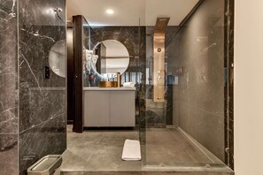A modern bathroom with a glass-enclosed shower, a vanity with a round mirror, and a towel on the floor. - w Charming Cozy 3BR in the Heart of Zona T (Bogotá)