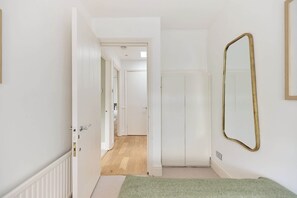 A hallway with a door leading to a room, a mirror on the wall, and a carpet. - The Two-Bedroom Edit (Greater London)