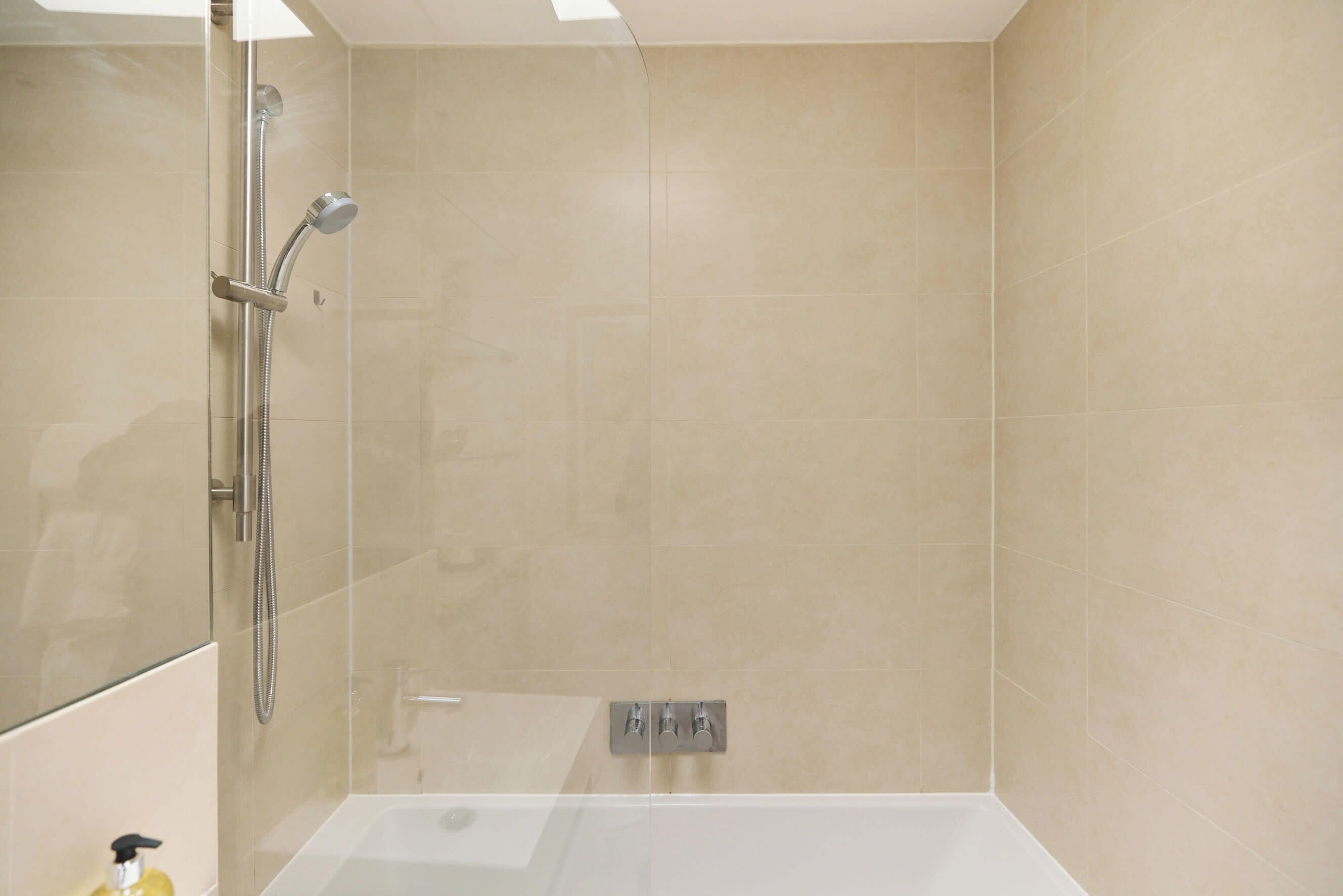 A modern bathroom with a glass-enclosed shower, a white bathtub, and a wall-mounted faucet.