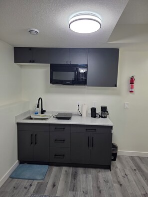 A modern kitchen with a built-in microwave, a coffee maker, and a fire extinguisher. - Marilyn’s Luxurious Basement Apartment (Saskatoon)