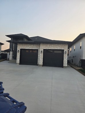 A modern two-story house with a stone facade and two black garage doors. - Marilyn’s Luxurious Basement Apartment (Saskatoon)