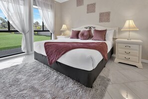 Une chambre à coucher comprenant un lit, des tables de chevet, une vue sur l’extérieur et des œuvres d’art décoratives au mur.