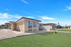 Une maison moderne à deux étages, dotée d’une façade en pierre, de grandes fenêtres et d’une pelouse bien entretenue.