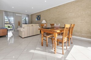 Uma sala de estar moderna com área de jantar, apresentando uma parede de tijolos, um sofá, uma mesa de jantar de madeira e um abajur.