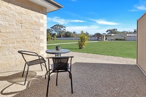 Un espace patio avec deux chaises et une table, un mur en briques et une vue sur un champ verdoyant et des arbres.