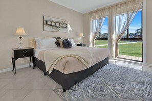 Une chambre à coucher avec un grand lit, deux tables de chevet, un tapis et une vue sur une pelouse par la fenêtre.